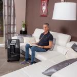 Der stationäre Sauerstoffkonzentrator Compact 525 steht im Wohnzimmer neben dem Sofa auf dem ein Mann sitzt und ein Buch liest.