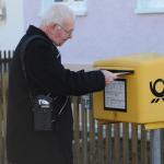 Ein älterer Herr wirft einen Brief in den Briefkasten. Über der Schulter trägt er den EasyMate.