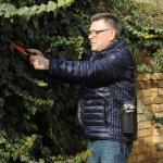 Ein Mann schneidet seine Hecke im Garten. Über der Schulter trägt er den EasyMate.