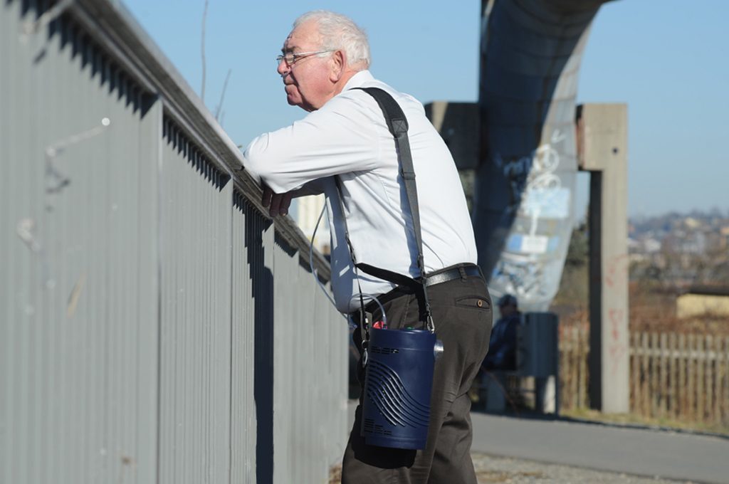 Ein Mann steht an einem Geländer, er trägt den Sprint auf der Schulter. mobile Flüssigsauerstoffgeräte
