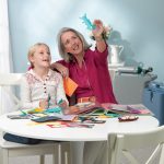 Eine Frau sitzt mit ihrer Enkelin am Tisch und bastelt. Im Hintergrung steht die Heimfüllanlage UltraFill mit einem EverFlo.