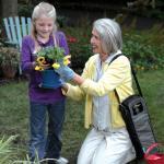 Eine Frau topft im Garten mit ihrer Enkelin Blumen um. Über der Schulter trägt sie die Sauerstoffflasche vom UltraFill.