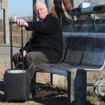 : Ein älterer Herr sitz auf einer Parkbank. Der iGo steht auf dem Boden neben ihm und er hält sich am Griff des Trolleys fest.
