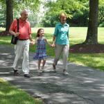 Oma und Opa spazieren mit dem Enkel durch einen Park. Der Opa trägt den Inogen One G5 auf seiner rechten Schulter. - Inogen One G5